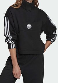 Svart kort sweatshirt med hög krage, vitt broderat logotyp och tre vita ränder på varje ärm. Mjuk tygkvalitet.