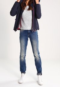 Navyblå polstret jakke med lyserød lynlås, hvid tekstureret skjorte, blå jeans og hvide sneakers. Outfittet har afslappede, moderne elementer.