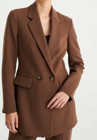 Brun dubbelknäppt kavaj, skräddarsydd passform, gjord av textilmaterial med struktur. Har spettslag, två knappar och framfickor.