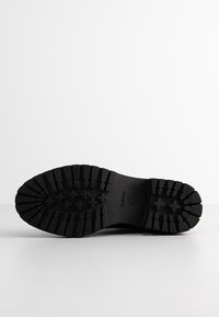 Semelle de bottes en caoutchouc noir avec des crampons profonds pour la traction, présentant des motifs circulaires et croisés, une texture lisse, et un logo Geox embossé.
