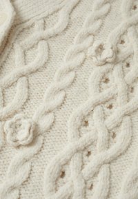 Cream-colored knitted fabric with raised cable patterns and small knit flowers woven into the design.