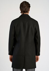 Abrigo de lana negro con una silueta larga, cuello ancho y costura trasera sutil. Presenta puños abotonados y una textura suave.