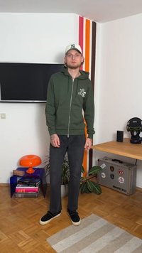 Grön zip-up hoodie med framfickor, svarta jeans och svarta slip-on skor. Hoodien har en logotyp på bröstet.