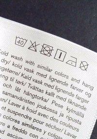 L’étiquette d’entretien indique lavage à 40°C, pas de blanchiment, pas de séchage en machine, séchage à plat, repassage à basse température, pas de symboles de nettoyage à sec avec instructions de lavage multilingues.