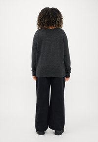 Suéter oversized cinza escuro com mangas longas, corte descontraído e punhos canelados, combinado com calças largas pretas e calçado preto.