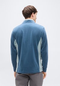 Φλις πουλόβερ σε μπλε με ανοιχτό μπλε τόνους, με ψηλό γιακά και μακριά μανίκια. Λείο υφή, άνετη εφαρμογή με καμπυλωτές πλαϊνές ραφές.