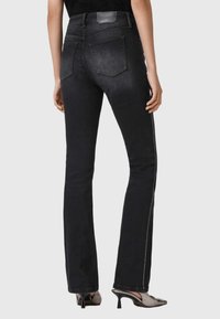 Zwarte uitlopende spijkerbroek met een taille op middelhoog niveau, vijf zakken en contrasterend witte zijstiksels. Het materiaal is denim met een gladde textuur.