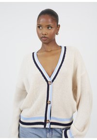 Cardigan lavorato a maglia in crema con dettagli a strisce blu e navy, caratterizzato da un profondo scollo a V e grandi bottoni in legno, vestibilità ampia e maniche lunghe.
