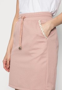 Falda tejida de color rosa con una superficie texturizada, que presenta una cintura con cordón, bolsillos y un acento trenzado en el borde del bolsillo.