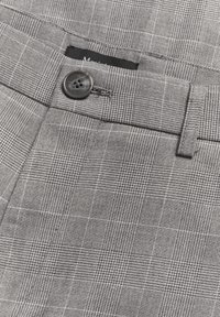 Pantalones grises con un diseño de cuadros texturizado, que presentan un botón negro y una cinturilla, además de un pequeño bolsillo sobre el botón.