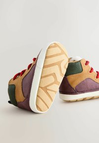 Kinderschuhe im Hochformat mit braunen, grünen und lila Panellen, roten Schnürsenkeln, weicher Sohle mit gemustertem Profil und weichem Innenfutter.
