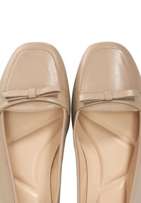 Ballerines en cuir beige avec un embout carré et un petit nœud décoratif à l'avant. L'intérieur présente un design texturé et profilé. Finition lisse.