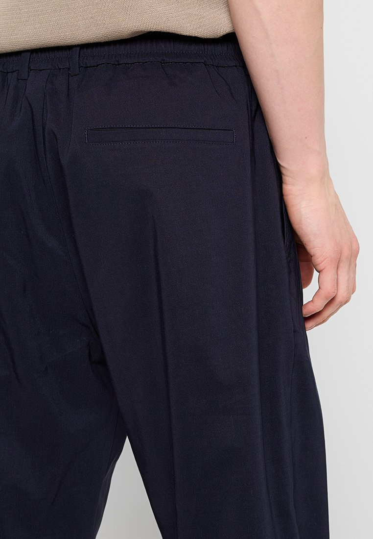 Granatowe spodnie z elastycznym pasem, z jedną tylną kieszenią i gładką teksturą materiału. Brak widocznych wzorów lub detalów metalowych.