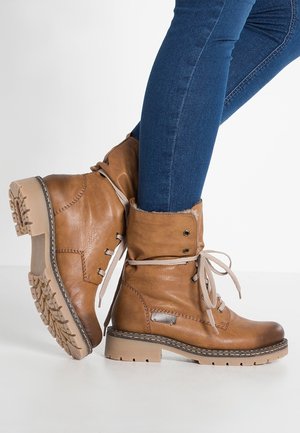 Bottines marron en cuir à lacets portées avec un jean bleu ajusté, un pied légèrement levé montrant la semelle extérieure robuste.