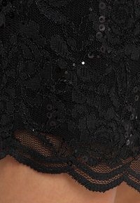 Svart spets tyg med blommönster och spridda paljetter. Sjö kanten är scalloped och visar en texturerad spetsdesign.