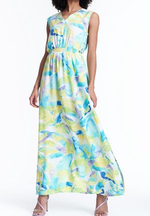 Vrouw draagt een mouweloze jurk met een V-hals, tot op de vloer, met een pastelblauw, groen en geel abstract bladerenpatroon en een elastische taille.