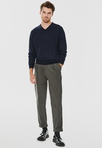 Granatowy sweter w serek w połączeniu z oliwkowymi spodniami, z mankietami na dole, oraz czarnymi sznurowanymi butami, tworzącymi czysty, minimalistyczny wygląd.