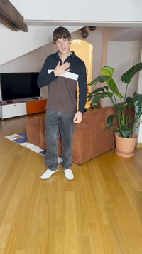 Zwarte en bruine longsleeve polo met witte band, gecombineerd met donkere jeans en witte sneakers. Staande in een kamer met planten en meubels.