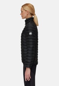 Zwarte pufferjack met horizontale stiksels, hoge kraag, zijzak met rits en logo op de linkermouw. Gladde, lichte stof.
