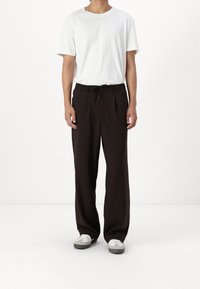 Brązowe spodnie o szerokich nogawkach z troczkiem w pasie, połączone z prostym, białym T-shirtem z krótkim rękawem. Szare sneakersy dopełniają strój.