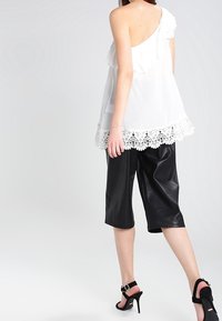 Top blanco con un tirante, diseño con volantes y dobladillo de encaje, combinado con culottes de imitación piel negra y sandalias de tacón alto.