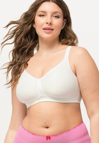 Soutien-gorge sans fil blanc en tissu lisse, au design en V et avec des bretelles réglables. Accompagné d'un sous-vêtement rayé rose et blanc avec un accent en nœud.