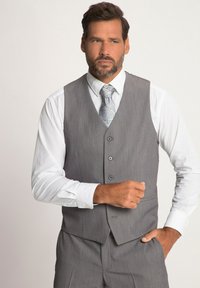 Chaleco gris con una tela texturizada, que presenta cinco botones y un cuello en punta, combinado con una camisa blanca y una corbata estampada.
