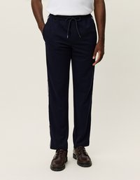 Námornícky modré športové nohavice vyrobené z mäkkej látky, navrhnuté s elastickým pásom a šnúrkou na sťahovanie. Obsahujú bočné pruhy a vrecká.