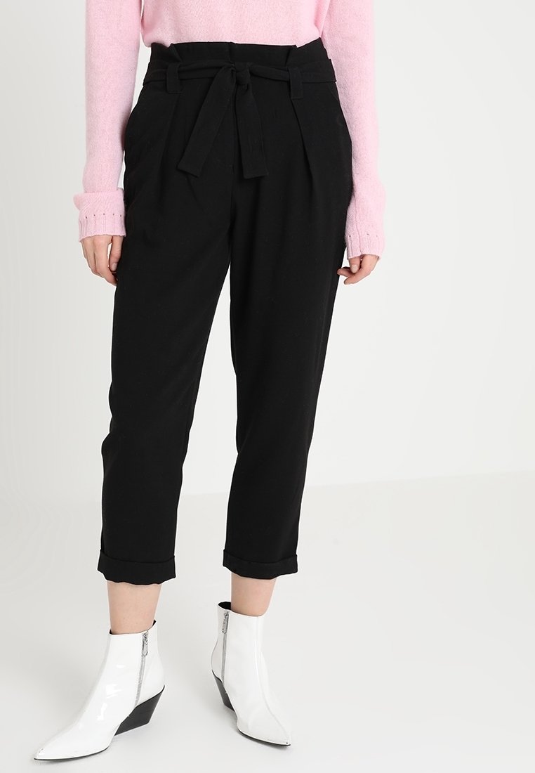Pantaloni neri su misura con cintura a cravatta, caratterizzati da pieghe e lunghezza cropped. Abbinati a stivali alla caviglia bianchi e angolari.