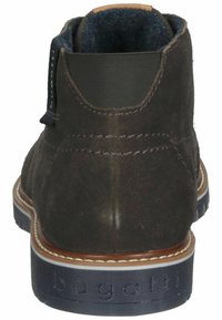 Bottines en daim brun foncé avec un talon légèrement surélevé, des panneaux latéraux élastiques et une semelle en caoutchouc bleue ornée d'un logo embossé.