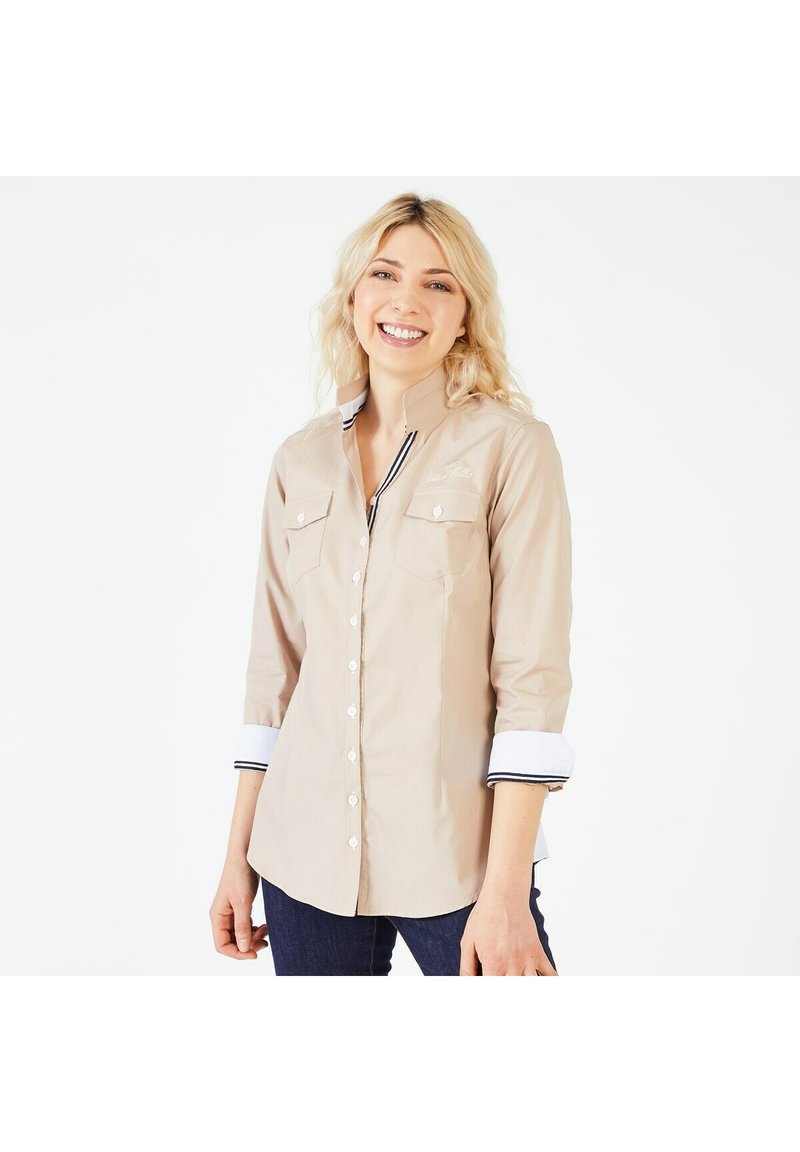 Chemise beige à manches longues avec col mandarin, devant boutonné blanc, poches poitrine et poignets rayés contrastés. Texture du tissu douce.