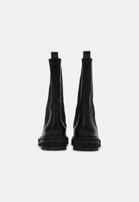 Mustat nahka nilkkakengät, joissa on sileä pinta, pystysaumat, vetonauhat takana ja paksu kumipohja, jossa on teksturoitu pito.