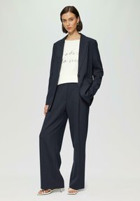Granatowa marynarka dopasowana na białym t-shircie z grafiką i napisem. Szerokie granatowe spodnie oraz srebrne sandały na obcasie dopełniają całość.