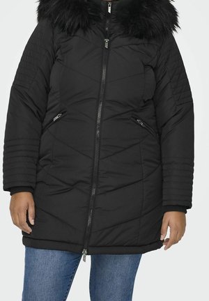 Zwarte gewatteerde winterjas met rits aan de voorkant en bontkraag, gedragen met een blauwe spijkerbroek, zichtbaar van schouders tot halverwege de dijen.