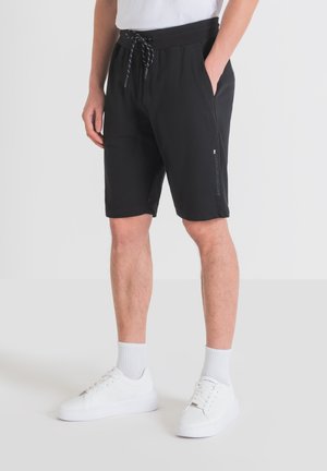 Shorts de sport noirs avec une taille élastique et un cordon de serrage. Comprend des poches latérales et un logo sur la jambe. Le tissu semble lisse et léger.