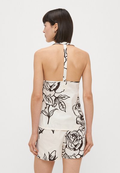 Top halter com padrão floral em creme, com flores contornadas a preto e um design de costas abertas. Combinado com calções combinando, apresentando o mesmo padrão.