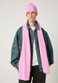 Roosa kudumine beanie, millel on tekstureeritud muster, koos pika roosa salliga, kantud valge särgi ja teksajaki üle.