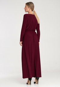 Długa burgundowa sukienka z długimi rękawami, elastycznym pasem i zwiewnym materiałem; w połączeniu z czarnymi szpilkami. Gładka faktura, minimalistyczny design.