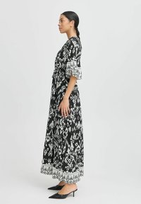 Maxikleid in Schwarz und Weiß, mit gemustertem Stoff, weit ausgestellten Ärmeln und Taillengebun. Glatte Textur mit dekorativen Akzenten am Saum.