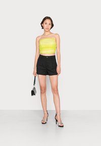 Top cropped sem alças de neon amarelo com tecido texturizado, combinado com calções pretos ajustados e sandálias de salto alto pretas com tiras.