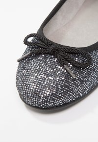 Ballerine noire avec dessus texturé pailleté, ornée d'un nœud tressé à l'avant et d'une doublure intérieure lisse.