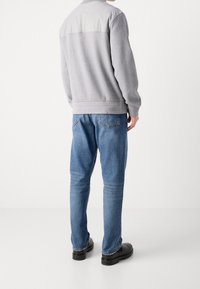 Gray sweatshirt with a light gray upper section, paired with blue denim jeans and black shoes. Soft texture and relaxed fit.