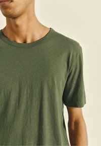 Olive green, short-sleeve crew neck t-shirt made from soft, textured fabric, featuring a relaxed fit and visible stitching details.