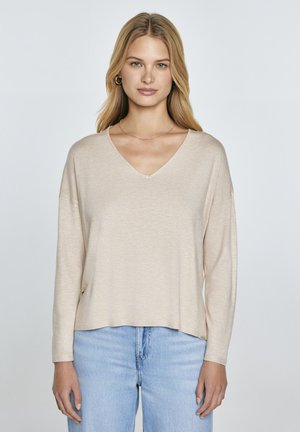 Beige långärmad Topp med V-ringning i ett lätt, mjukt material. Har en avslappnad passform och subtilt texturerad yta. Matchas med ljusblå jeans.