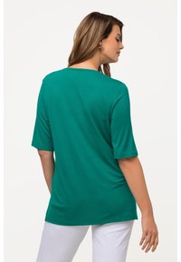 T-shirt in cotone color teal con maniche corte, vestibilità rilassata e scollatura rotonda, mostrato dalla parte posteriore, abbinato a pantaloni bianchi.