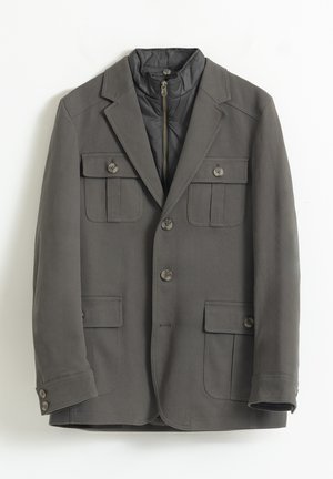 Blazer gris con una capa interna acolchada y con cremallera. Presenta dos bolsillos en el pecho, dos bolsillos frontales y cierres de botón. Textura suave.