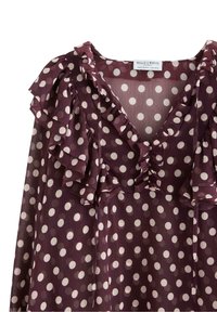 Burgundská blůza s bílými puntíky, která má volánkový límec a rukávy, představující ženský a hravý styl.