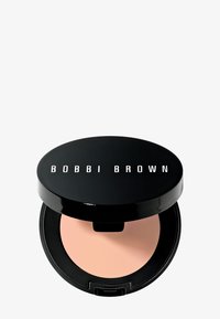 Compatta nera con finitura lucida e testo "BOBBI BROWN" sul coperchio. All'interno, una polvere rosa chiaro. Forma circolare con una sottile luce riflessa.