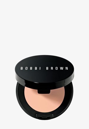 Compatta nera con finitura lucida e testo "BOBBI BROWN" sul coperchio. All'interno, una polvere rosa chiaro. Forma circolare con una sottile luce riflessa.