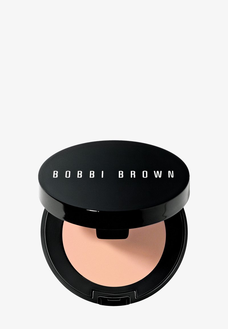 Compatta nera con finitura lucida e testo "BOBBI BROWN" sul coperchio. All'interno, una polvere rosa chiaro. Forma circolare con una sottile luce riflessa.